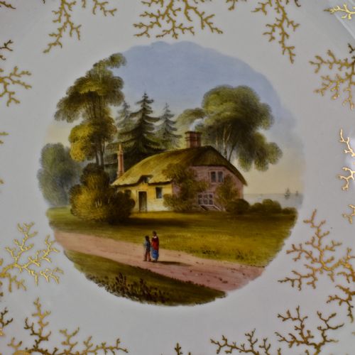 fig 2. A Regency porcelain dessert plate featuring a hand-painted central landscape surrounded by intricate gold gilt seaweed patterns on a scalloped white border.