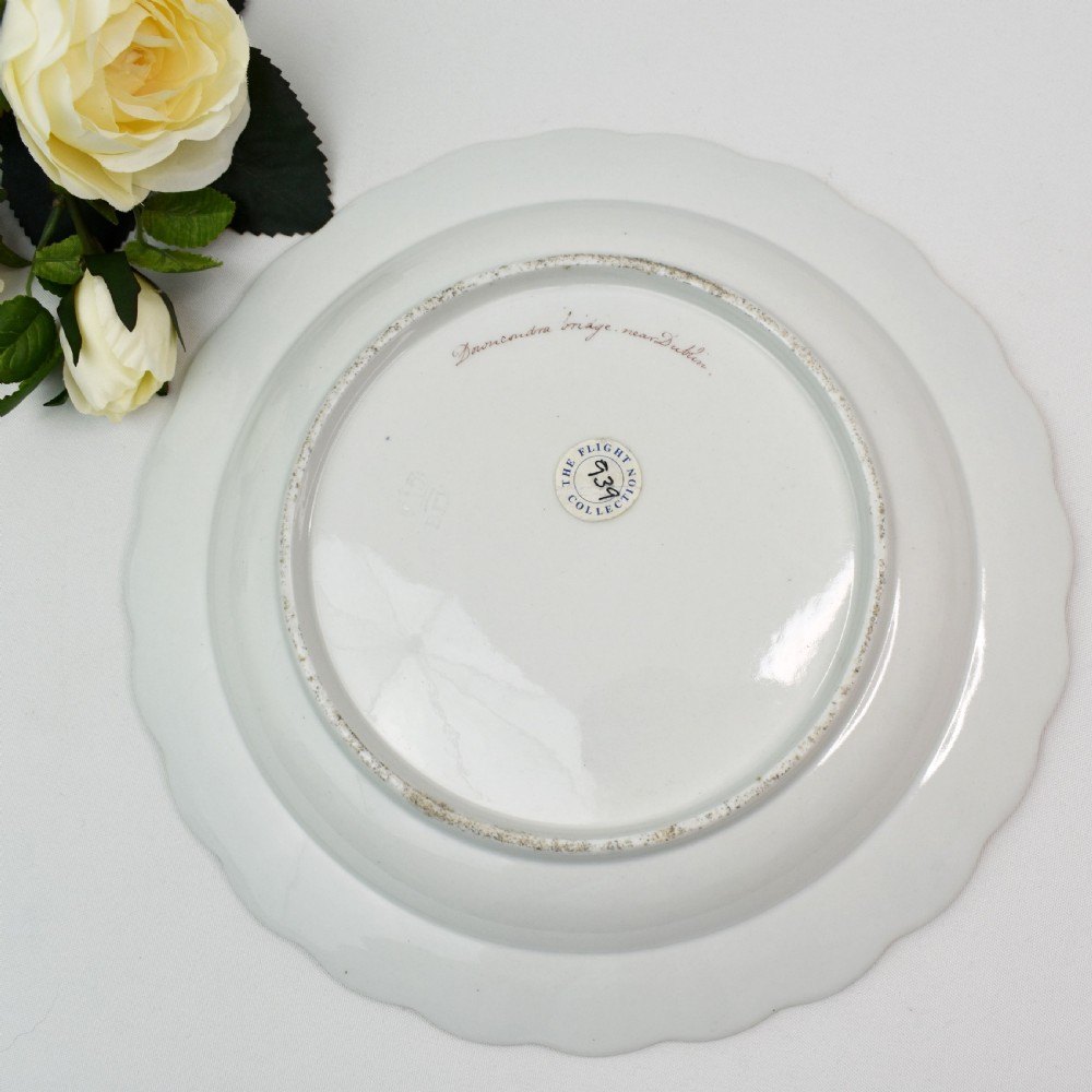 An antique circular porcelain plate featuring a scalloped gilded rim, cobalt blue border, hand-painted fruit and bird motifs, and a central landscape roundel. View VII
