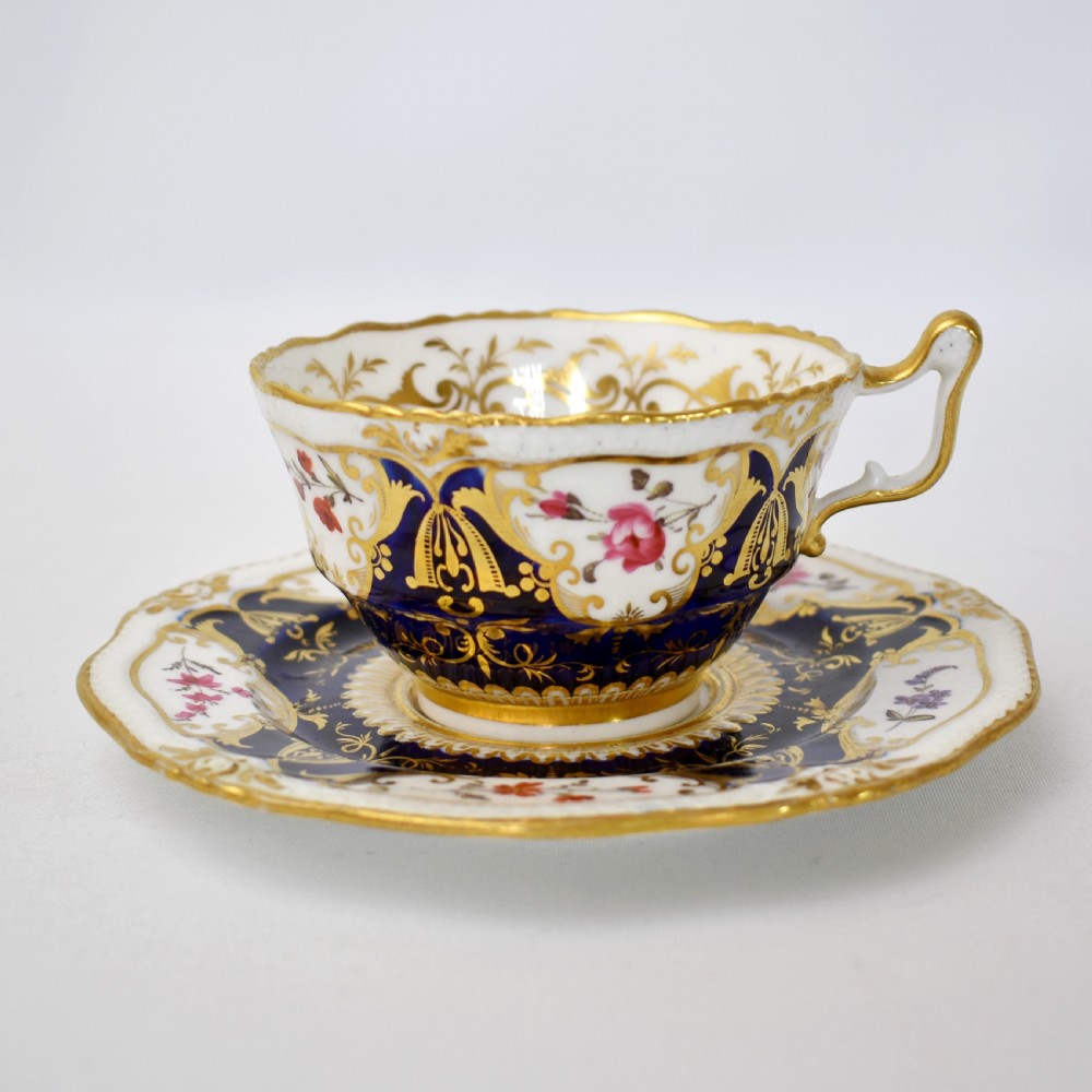 An antique porcelain teacup and saucer decorated with deep cobalt blue panels, floral hand-painted vignettes, and gold gilding.