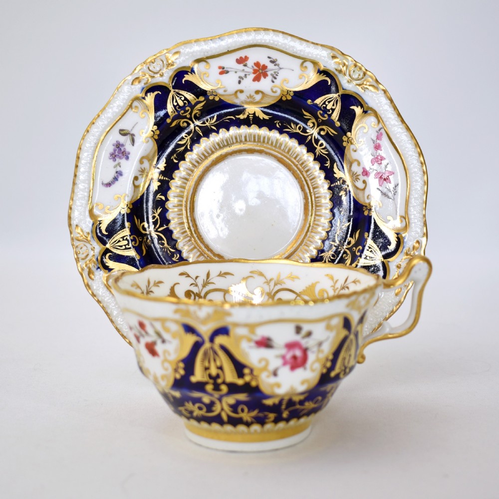 An antique porcelain teacup and saucer decorated with deep cobalt blue panels, floral hand-painted vignettes, and gold gilding. View II