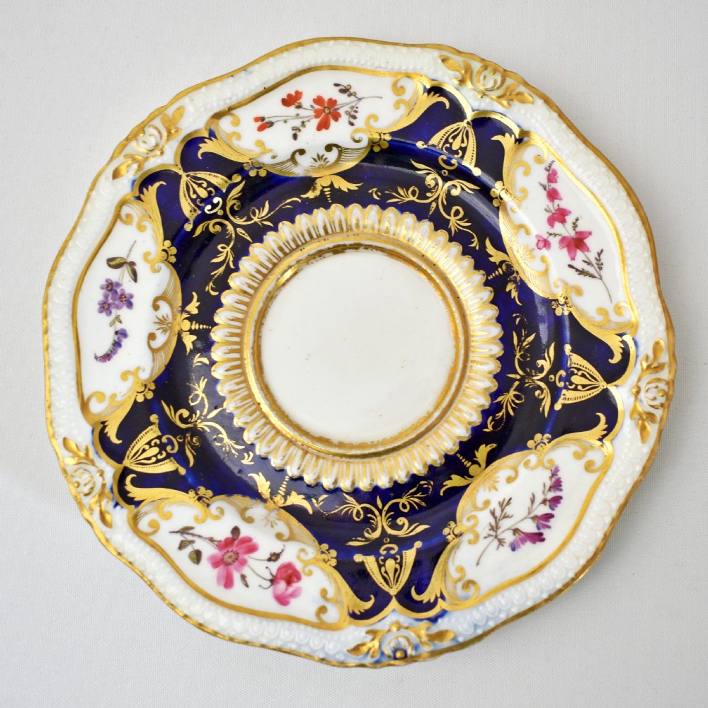 An antique porcelain teacup and saucer decorated with deep cobalt blue panels, floral hand-painted vignettes, and gold gilding. View III