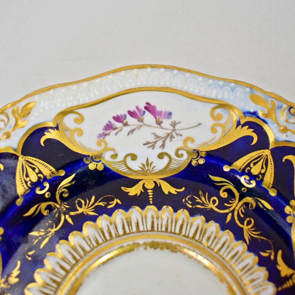 An antique porcelain teacup and saucer decorated with deep cobalt blue panels, floral hand-painted vignettes, and gold gilding. View VIII