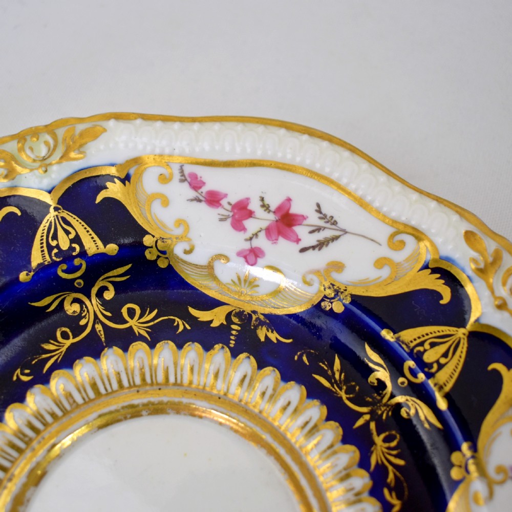 An antique porcelain teacup and saucer decorated with deep cobalt blue panels, floral hand-painted vignettes, and gold gilding. View IX
