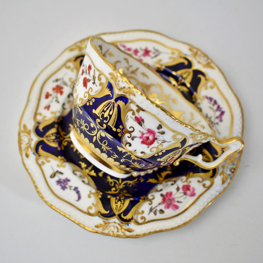 An antique porcelain teacup and saucer decorated with deep cobalt blue panels, floral hand-painted vignettes, and gold gilding. View X
