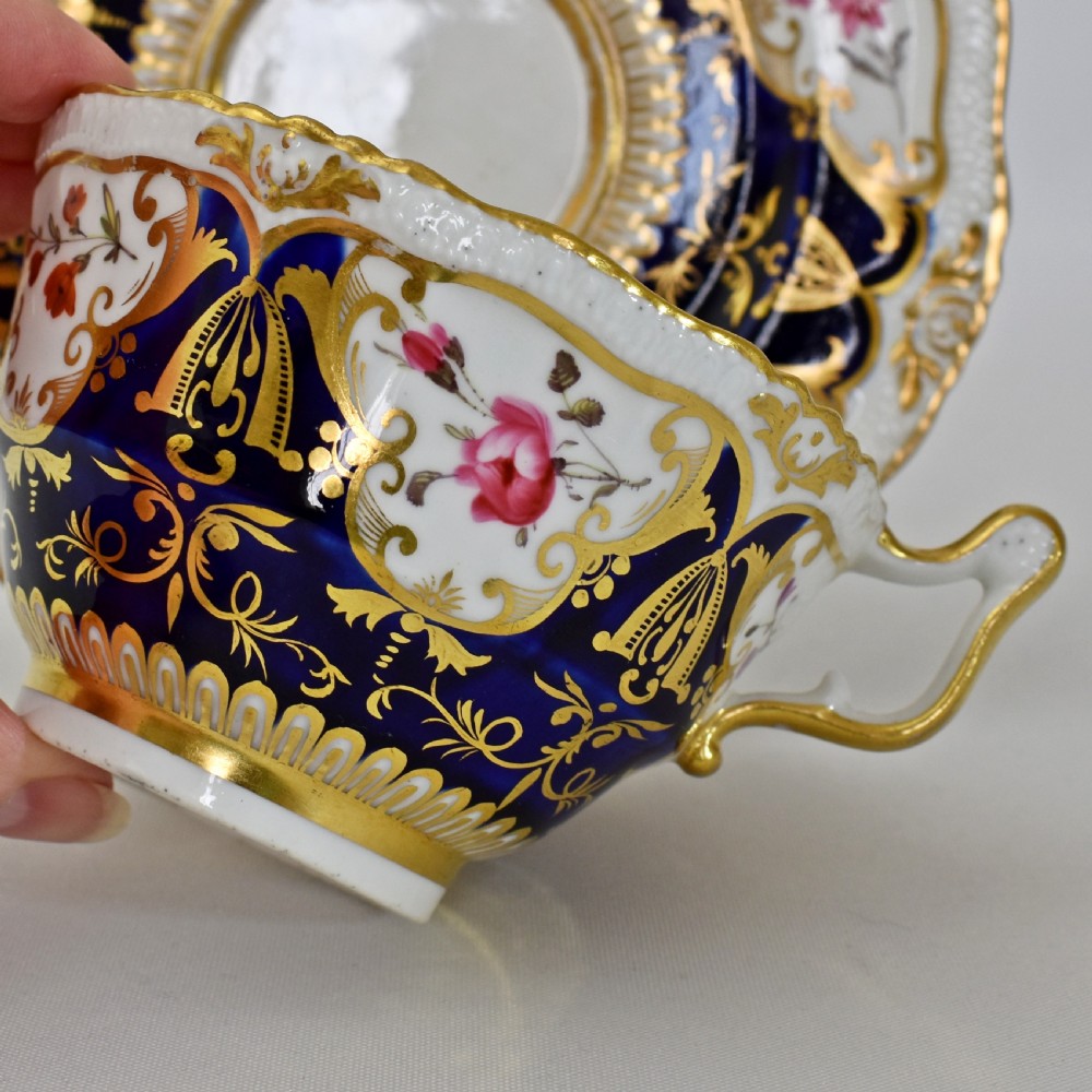 An antique porcelain teacup and saucer decorated with deep cobalt blue panels, floral hand-painted vignettes, and gold gilding. View XI