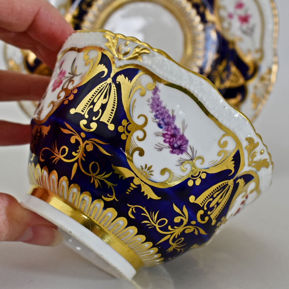 An antique porcelain teacup and saucer decorated with deep cobalt blue panels, floral hand-painted vignettes, and gold gilding. View XIII