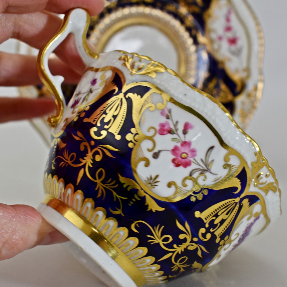 An antique porcelain teacup and saucer decorated with deep cobalt blue panels, floral hand-painted vignettes, and gold gilding. View XIV