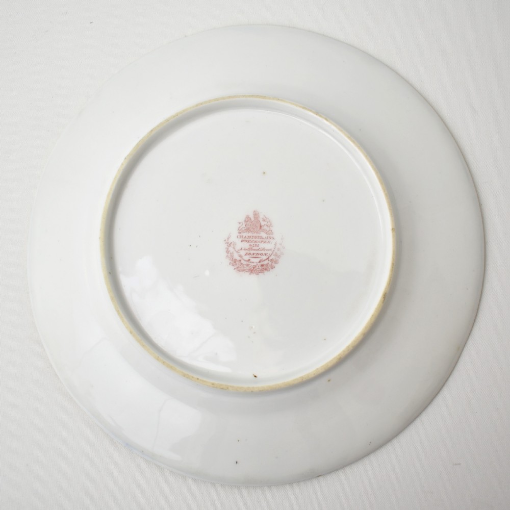 A circular porcelain dessert plate featuring a cobalt blue rim with six gilt-framed reserves depicting hand-painted pink roses around a central family coat of arms. View XI