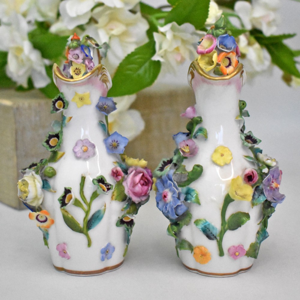 A pair of white Minton porcelain scent bottle ewers featuring applied three-dimensional flowers, gilded scroll handles, and matching floral stoppers. View II
