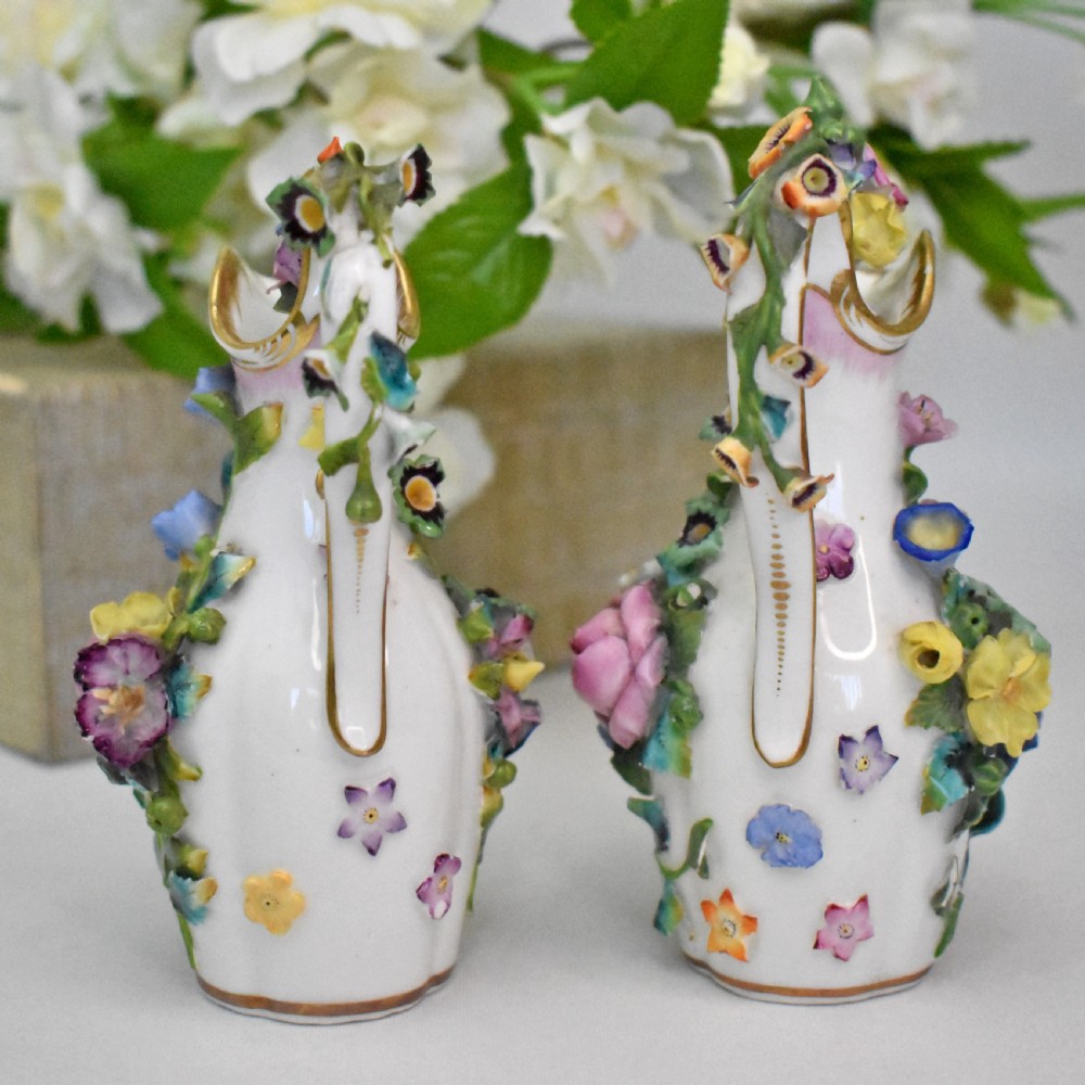 A pair of white Minton porcelain scent bottle ewers featuring applied three-dimensional flowers, gilded scroll handles, and matching floral stoppers. View III