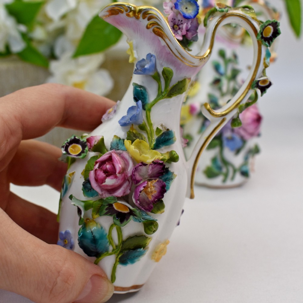 A pair of white Minton porcelain scent bottle ewers featuring applied three-dimensional flowers, gilded scroll handles, and matching floral stoppers. View VII