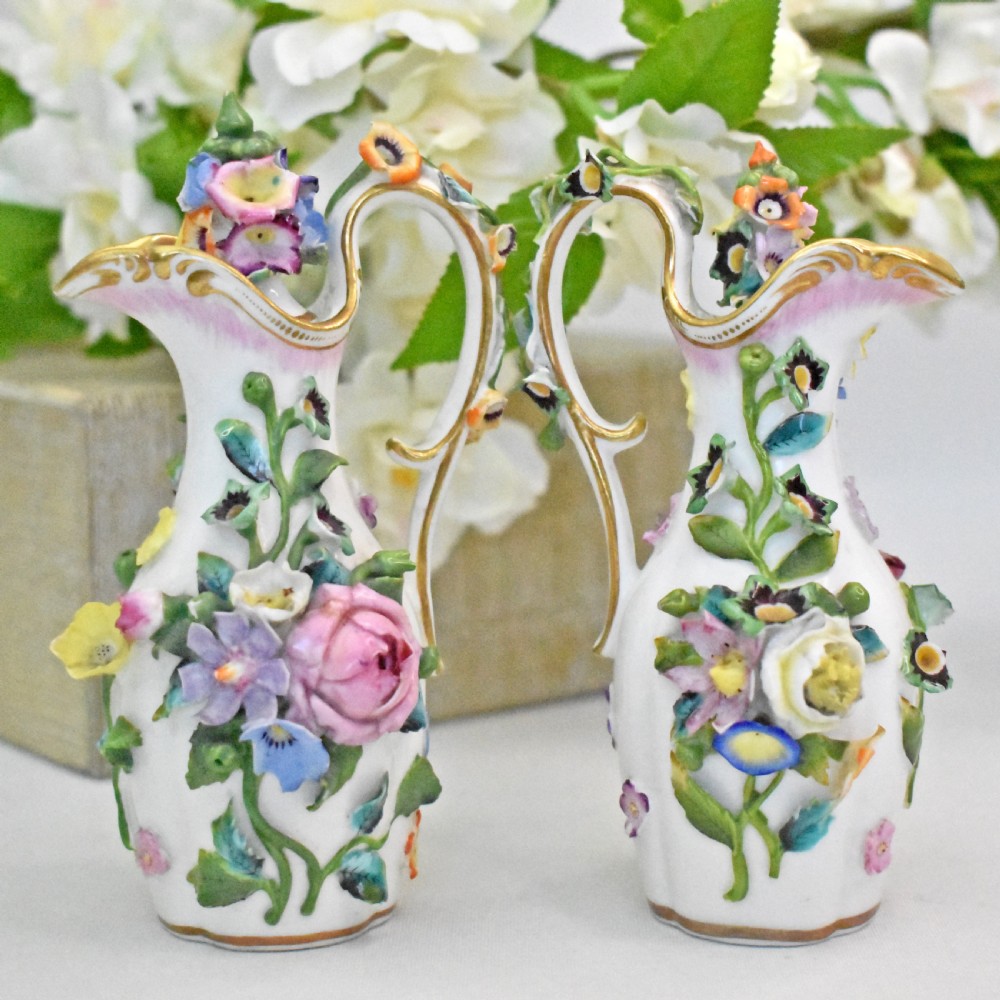 A pair of white Minton porcelain scent bottle ewers featuring applied three-dimensional flowers, gilded scroll handles, and matching floral stoppers. View XI
