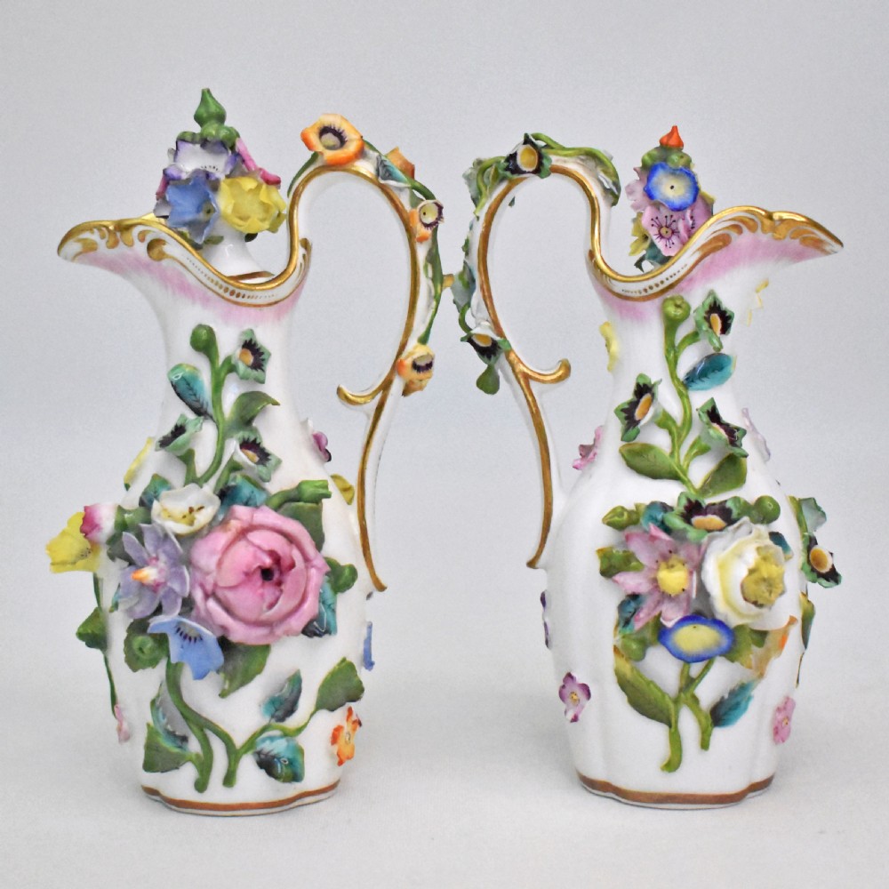 A pair of white Minton porcelain scent bottle ewers featuring applied three-dimensional flowers, gilded scroll handles, and matching floral stoppers. View XII