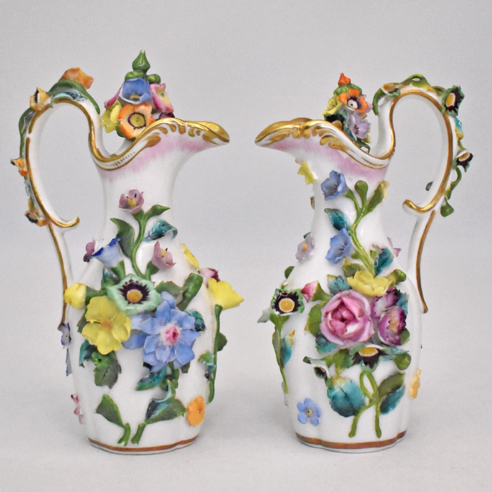 A pair of white Minton porcelain scent bottle ewers featuring applied three-dimensional flowers, gilded scroll handles, and matching floral stoppers. View XIV