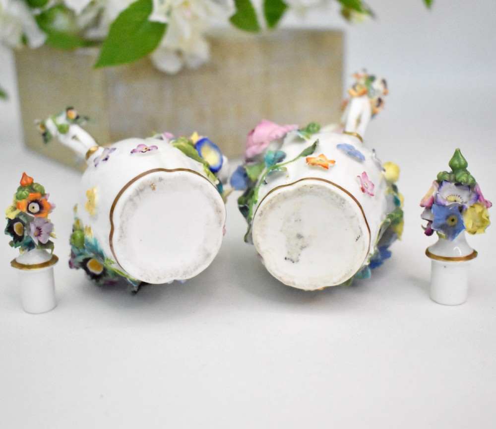 A pair of white Minton porcelain scent bottle ewers featuring applied three-dimensional flowers, gilded scroll handles, and matching floral stoppers. View XV