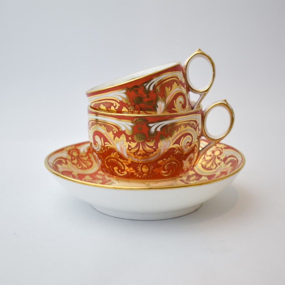 A Victorian Davenport porcelain true trio featuring a stacked tea cup and coffee cup decorated with intricate hand-painted rust red and gold ornamentation resting on a matching saucer.