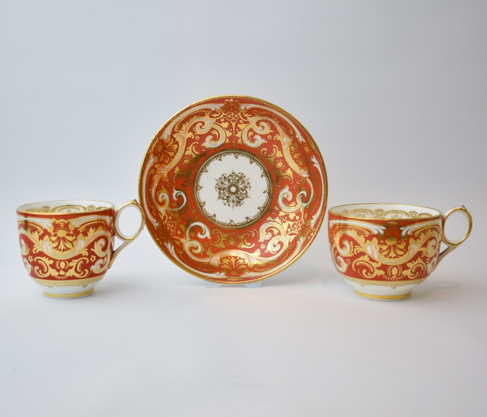 A Victorian Davenport porcelain true trio featuring a stacked tea cup and coffee cup decorated with intricate hand-painted rust red and gold ornamentation resting on a matching saucer. View II