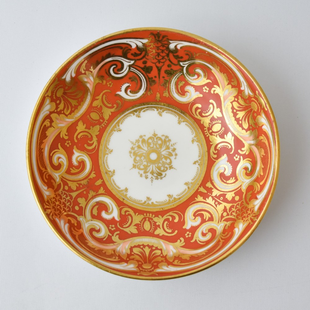 A Victorian Davenport porcelain true trio featuring a stacked tea cup and coffee cup decorated with intricate hand-painted rust red and gold ornamentation resting on a matching saucer. View V