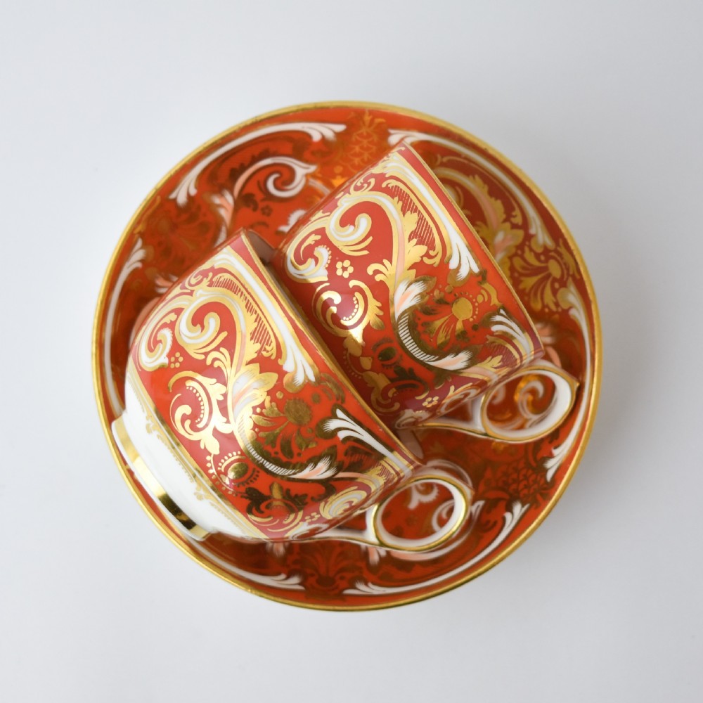 A Victorian Davenport porcelain true trio featuring a stacked tea cup and coffee cup decorated with intricate hand-painted rust red and gold ornamentation resting on a matching saucer. View VI