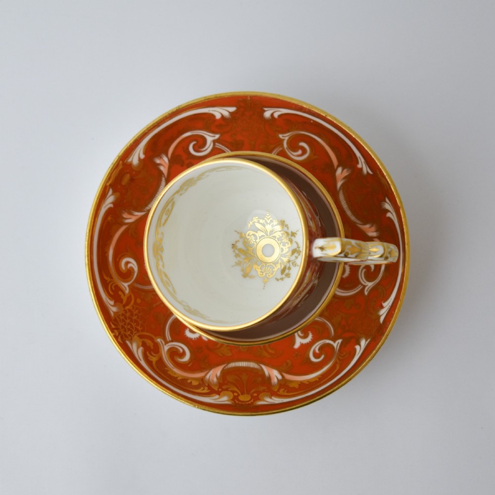 A Victorian Davenport porcelain true trio featuring a stacked tea cup and coffee cup decorated with intricate hand-painted rust red and gold ornamentation resting on a matching saucer. View VII