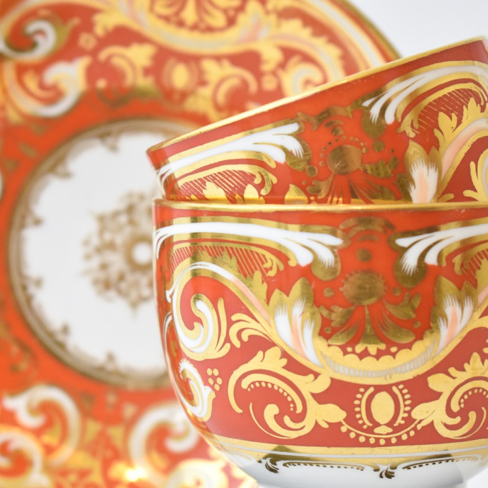 A Victorian Davenport porcelain true trio featuring a stacked tea cup and coffee cup decorated with intricate hand-painted rust red and gold ornamentation resting on a matching saucer. View VIII