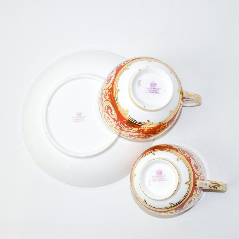 A Victorian Davenport porcelain true trio featuring a stacked tea cup and coffee cup decorated with intricate hand-painted rust red and gold ornamentation resting on a matching saucer. View IX