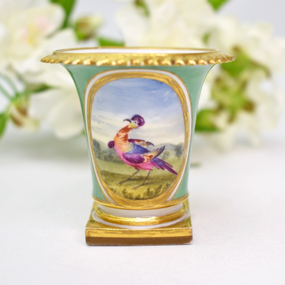 A miniature green Regency porcelain vase featuring a hand-painted exotic bird vignette framed in gold gilding upon a square pedestal base.