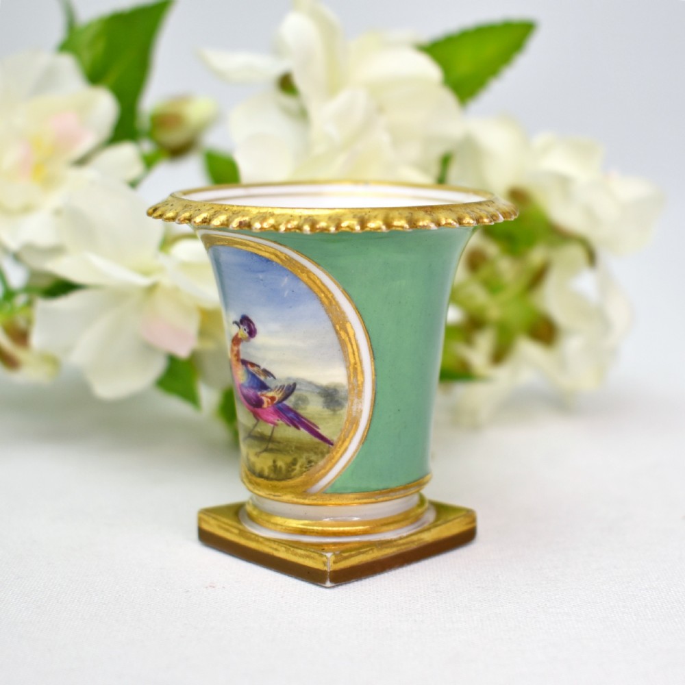 A miniature green Regency porcelain vase featuring a hand-painted exotic bird vignette framed in gold gilding upon a square pedestal base. View II