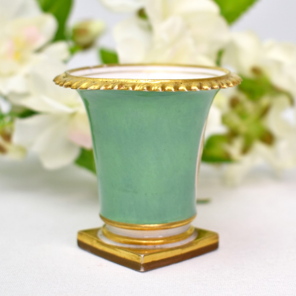 A miniature green Regency porcelain vase featuring a hand-painted exotic bird vignette framed in gold gilding upon a square pedestal base. View IV