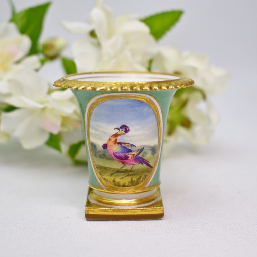 A miniature green Regency porcelain vase featuring a hand-painted exotic bird vignette framed in gold gilding upon a square pedestal base. View V