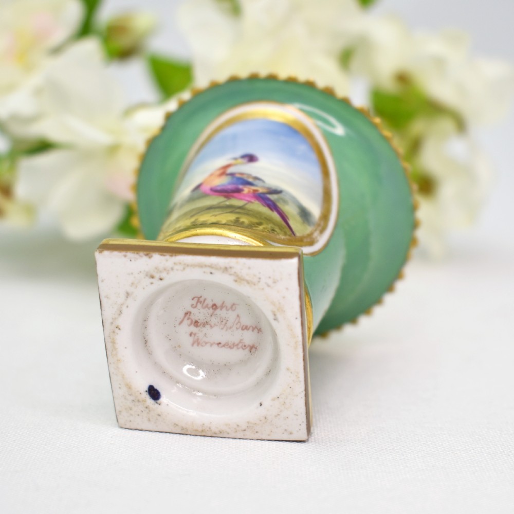 A miniature green Regency porcelain vase featuring a hand-painted exotic bird vignette framed in gold gilding upon a square pedestal base. View VIII