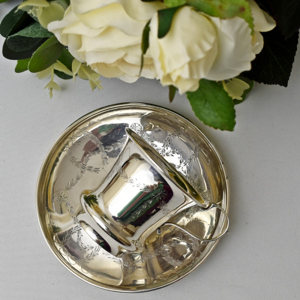 An antique sterling silver cup and saucer set decorated with hand-engraved swag and bow motifs. View III