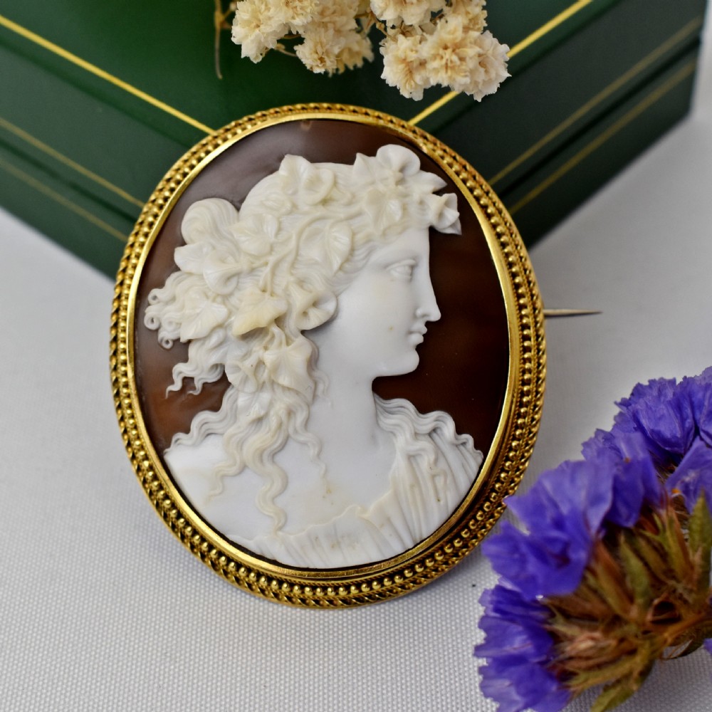 An oval Victorian cameo brooch featuring a white carved relief profile of Goddess Flora set within an 18ct gold frame with a twisted wire border.