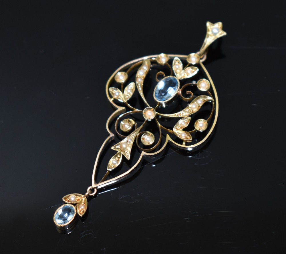 An openwork 15ct gold Art Nouveau pendant featuring intricate leaf motifs, set with seed pearls, a central oval aquamarine, and a suspended aquamarine drop.