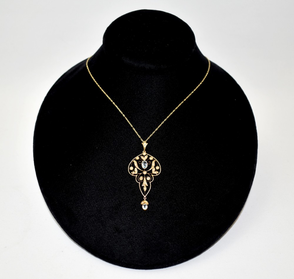 An openwork 15ct gold Art Nouveau pendant featuring intricate leaf motifs, set with seed pearls, a central oval aquamarine, and a suspended aquamarine drop. View V