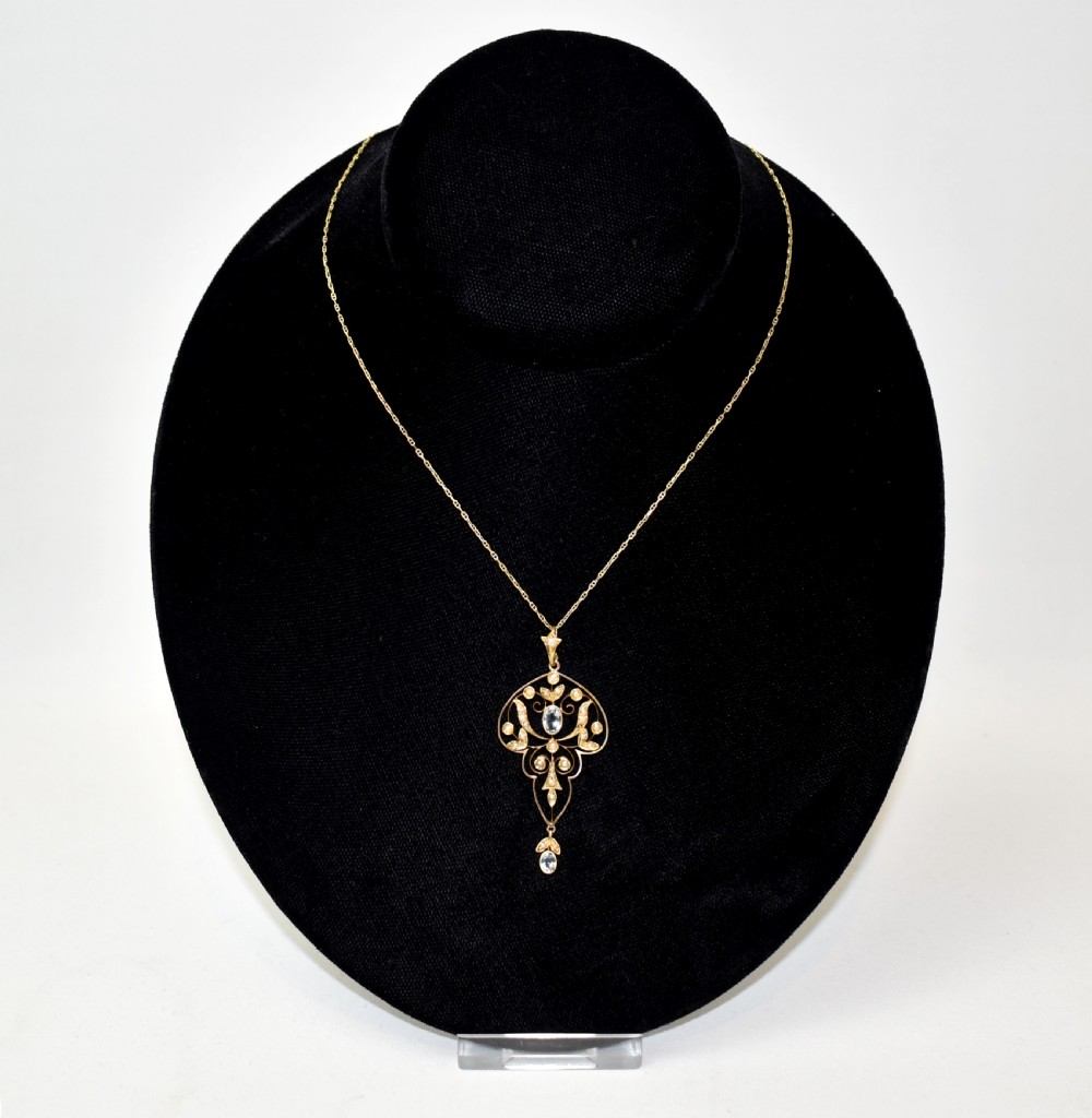 An openwork 15ct gold Art Nouveau pendant featuring intricate leaf motifs, set with seed pearls, a central oval aquamarine, and a suspended aquamarine drop. View IX