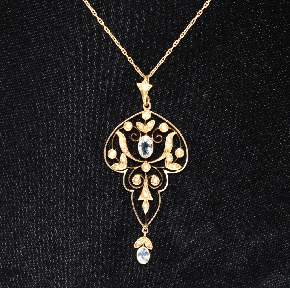 An openwork 15ct gold Art Nouveau pendant featuring intricate leaf motifs, set with seed pearls, a central oval aquamarine, and a suspended aquamarine drop. View X