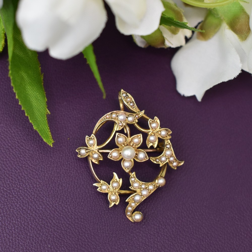 An Edwardian 15ct yellow gold floral brooch pendant featuring openwork scrollwork set with seed pearls.