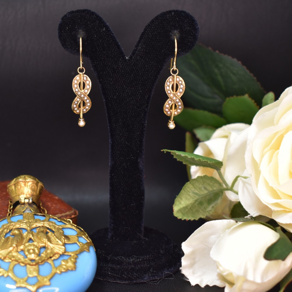 A pair of Edwardian gold drop earrings featuring figure-eight infinity loops set with seed pearls, displayed inside a blue velvet presentation box. View II
