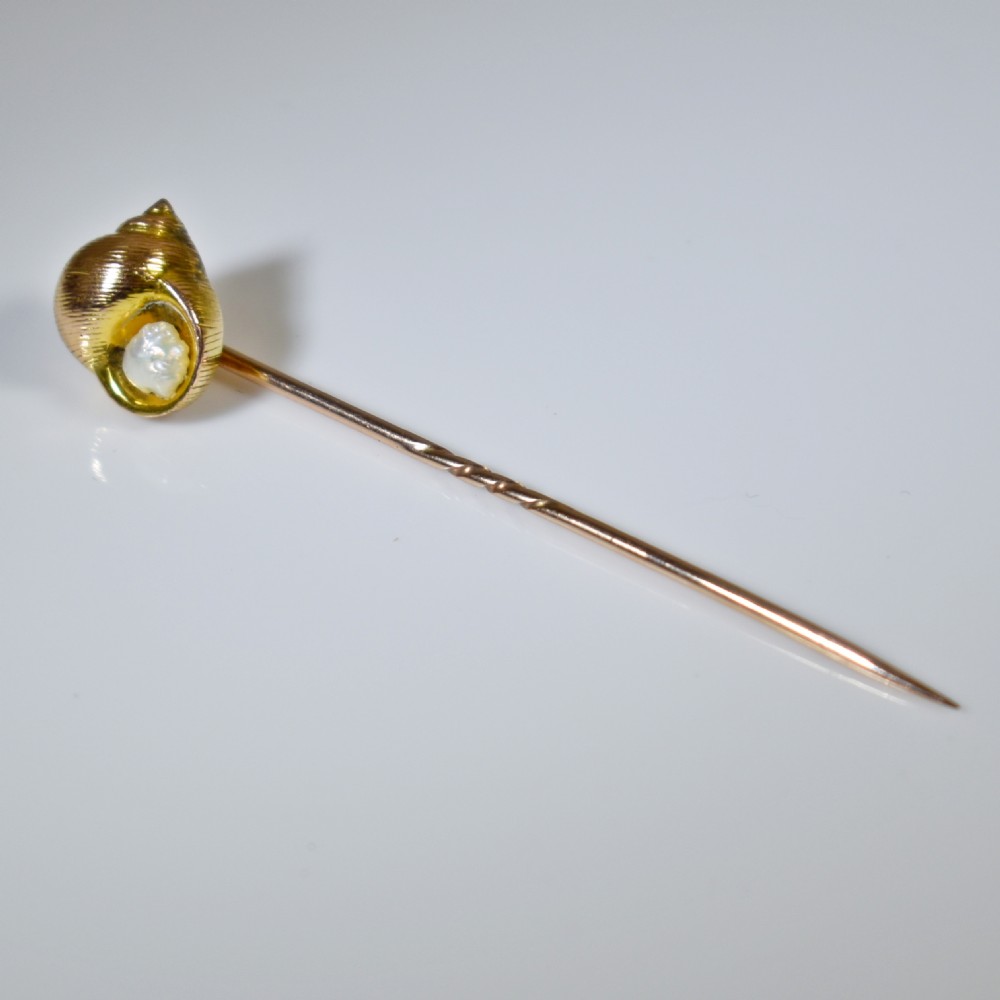 An Edwardian yellow gold stick pin featuring a textured shell casing enclosing a natural baroque pearl. View VI