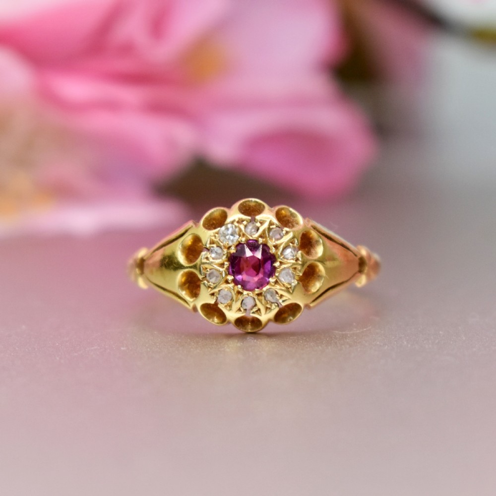 An 18ct yellow gold Edwardian ring featuring a central round ruby encircled by diamond accents set into a carved head band. View II