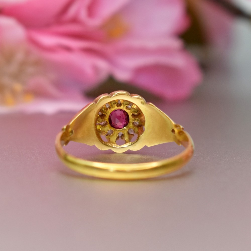 An 18ct yellow gold Edwardian ring featuring a central round ruby encircled by diamond accents set into a carved head band. View VII