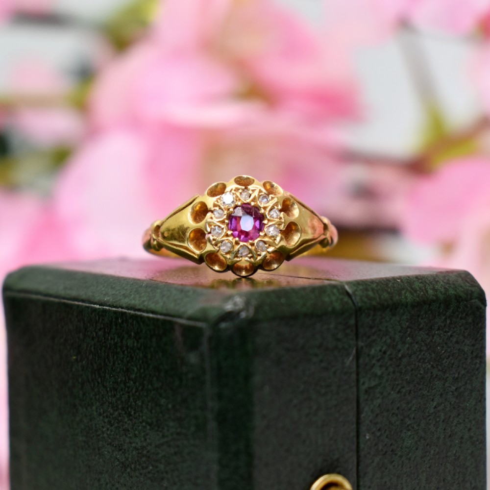 An 18ct yellow gold Edwardian ring featuring a central round ruby encircled by diamond accents set into a carved head band. View VIII