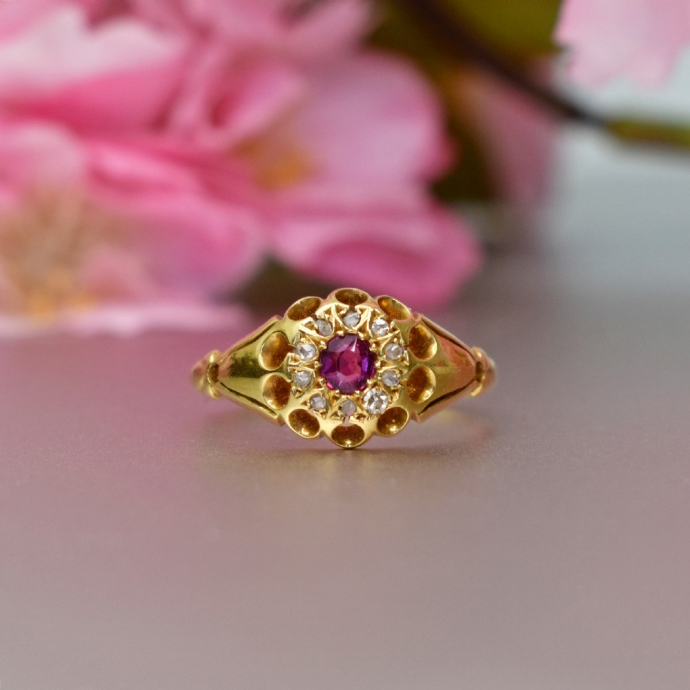 An 18ct yellow gold Edwardian ring featuring a central round ruby encircled by diamond accents set into a carved head band. View IX