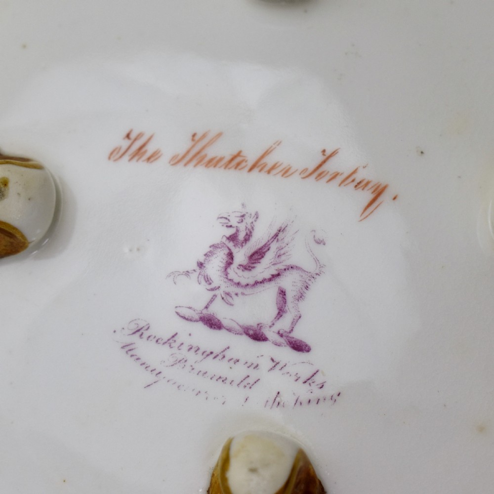 A circular Rockingham porcelain basket featuring applied botanical flowers, a branch-formed gilded handle, and a hand-painted landscape scene at the centre. View IX