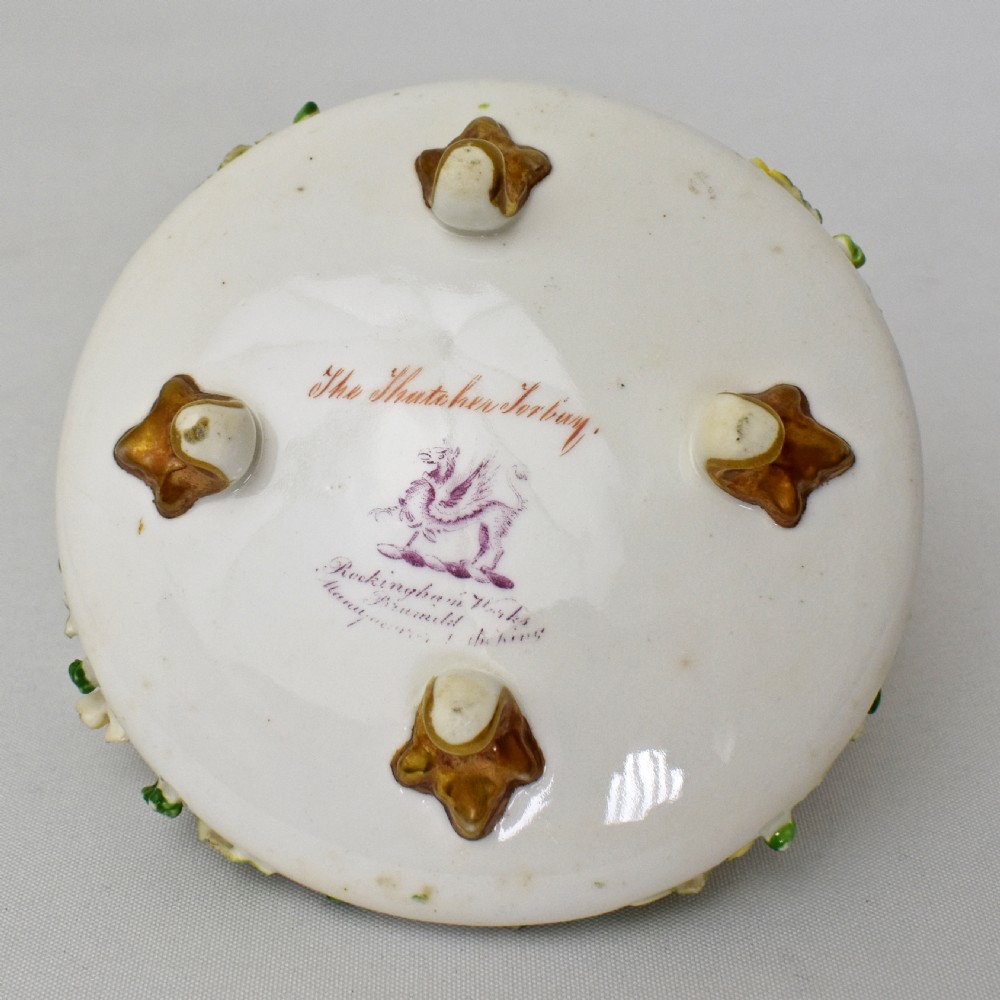A circular Rockingham porcelain basket featuring applied botanical flowers, a branch-formed gilded handle, and a hand-painted landscape scene at the centre. View XII