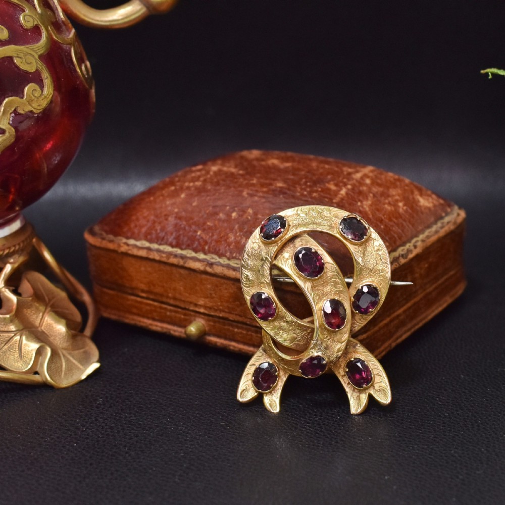 A Victorian 15ct gold brooch styled as an intertwined ribbon loop, textured with hand engraving and set with oval flat-cut almandine garnets. View II