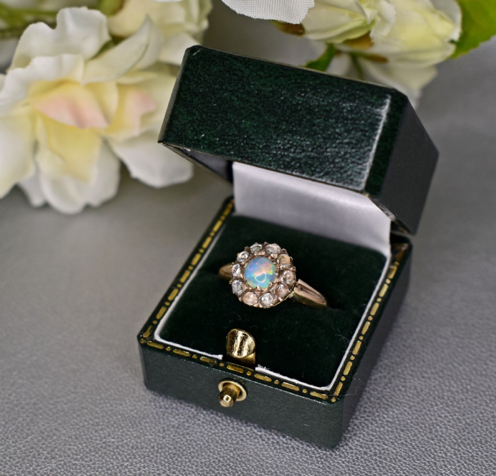 An antique gold Victorian cluster ring featuring a central cabochon opal surrounded by a halo of rose-cut diamonds, displayed inside a green velvet ring box.