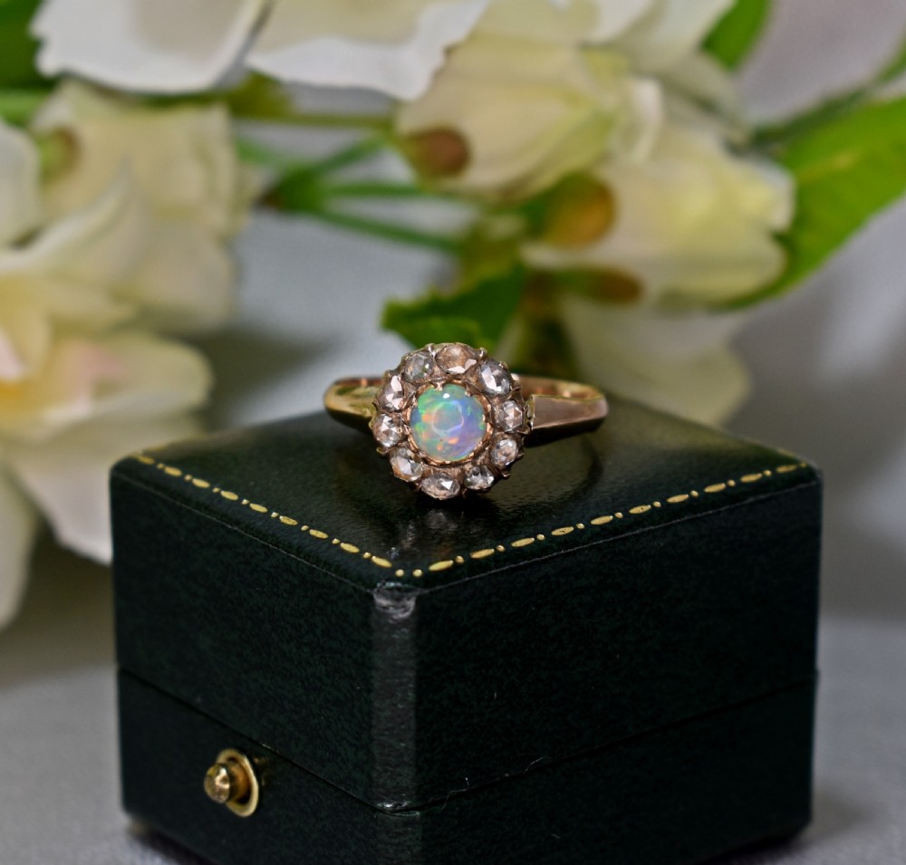 An antique gold Victorian cluster ring featuring a central cabochon opal surrounded by a halo of rose-cut diamonds, displayed inside a green velvet ring box. View II