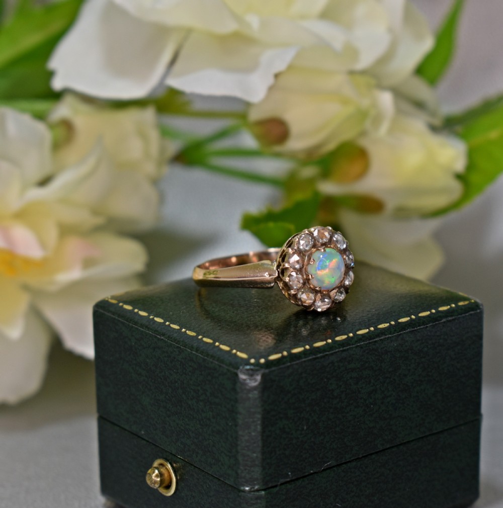 An antique gold Victorian cluster ring featuring a central cabochon opal surrounded by a halo of rose-cut diamonds, displayed inside a green velvet ring box. View III